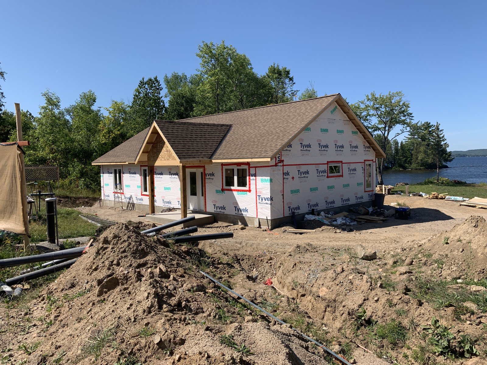 The home framed and roofed, on a waterfront lot with the lake directly behind it, utilities being laid.