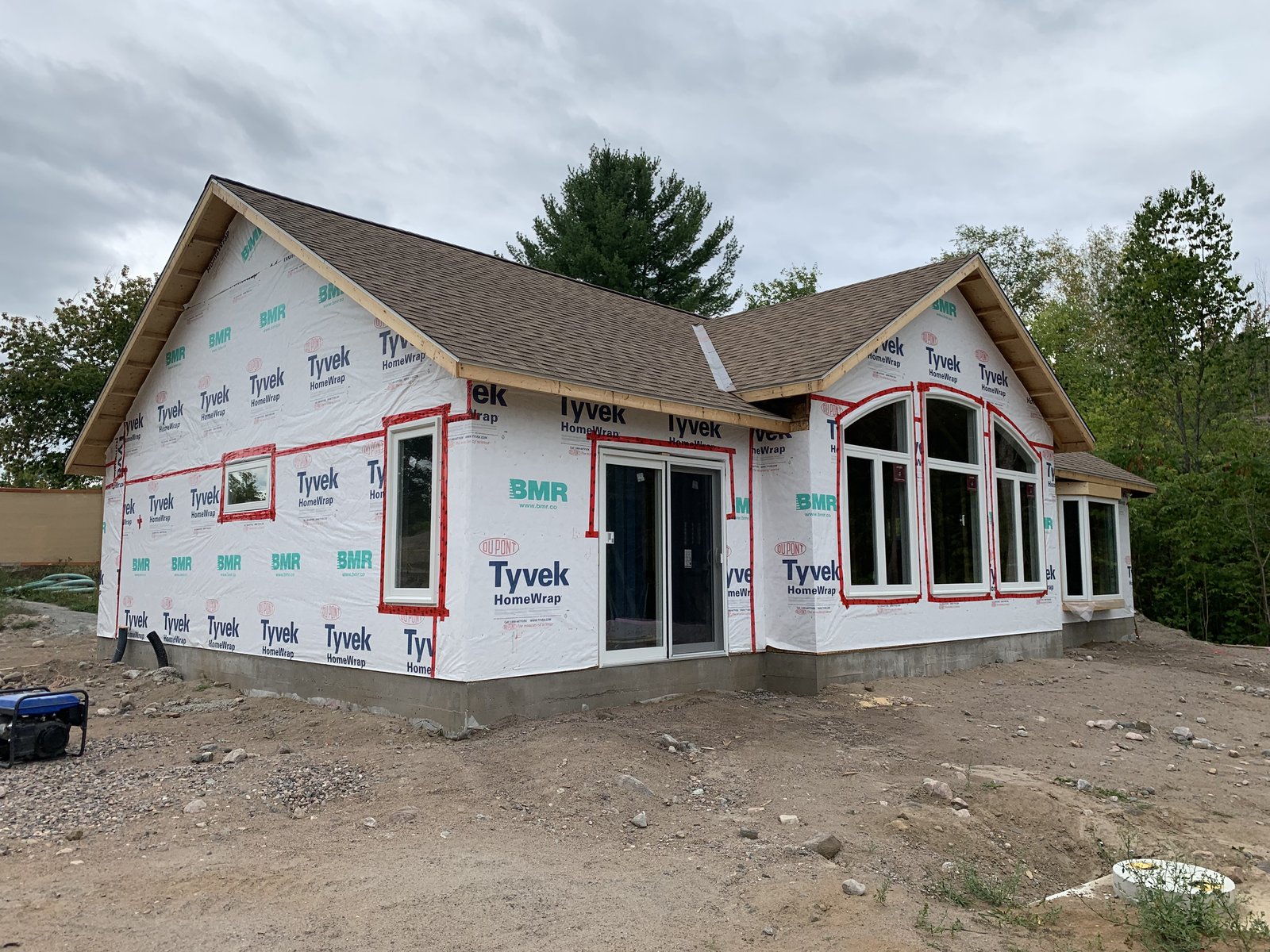 The home fully framed and roofed, Tyvek HomeWrap on and taped, windows installed, siding not yet started.