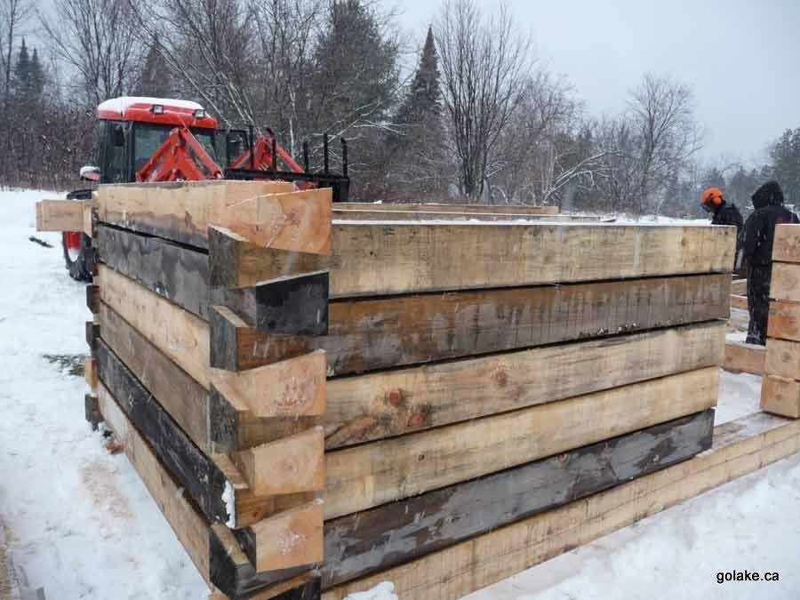 A log cabin under construction in winter at the Goldenville resort, dovetail-notched corners, the resort's own 