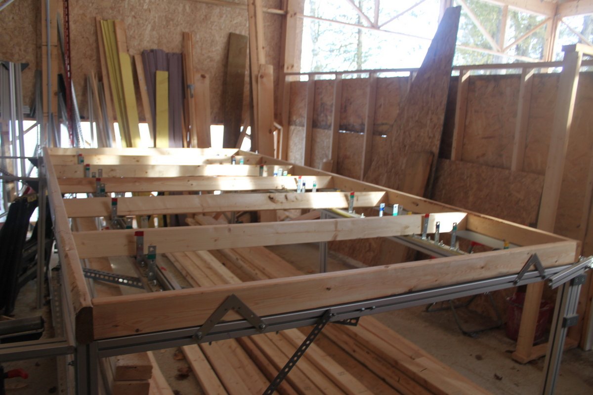 A full wall panel framed flat on the table apparatus, aluminum extrusion rails visible beneath the lumber, on an actual construction site.